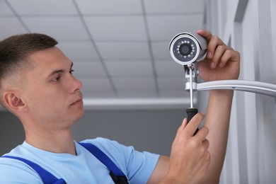 Photo of Technician with screwdriver installing CCTV camera on wall indoors