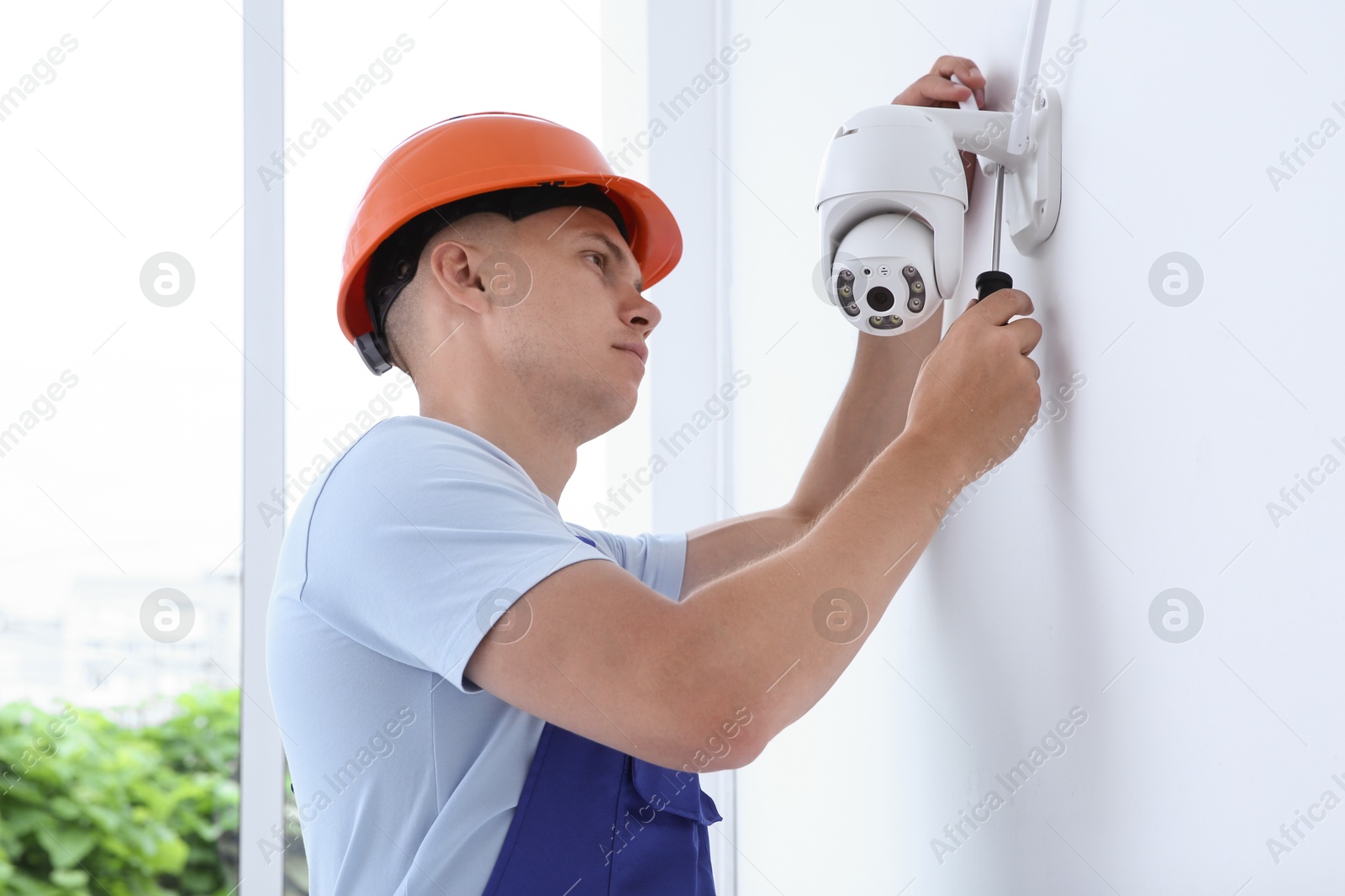 Photo of Technician with screwdriver installing CCTV camera on wall indoors