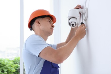 Technician with screwdriver installing CCTV camera on wall indoors