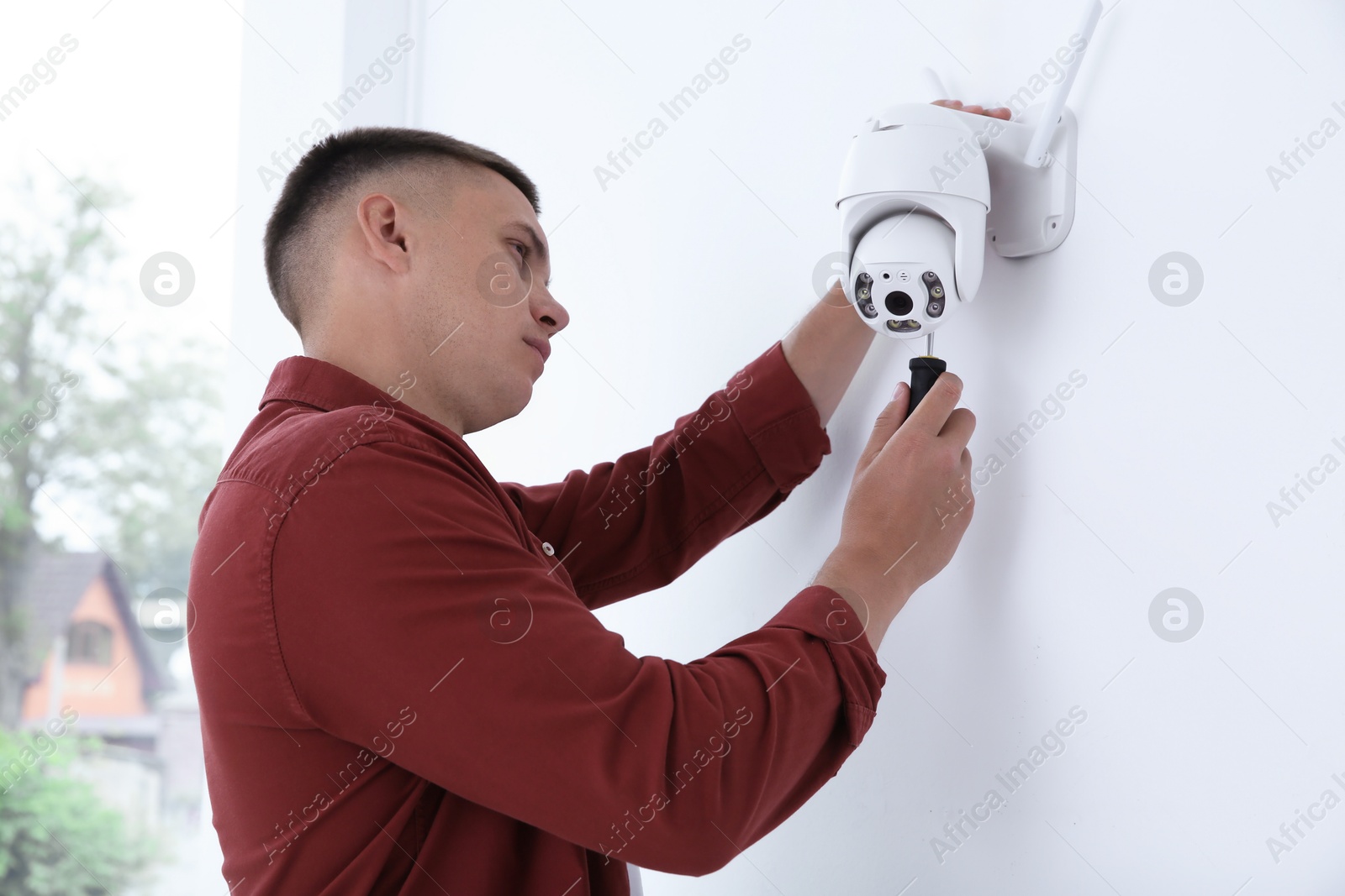 Photo of Technician with screwdriver installing CCTV camera on wall indoors