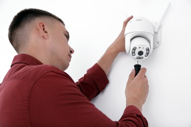 Technician with screwdriver installing CCTV camera on wall indoors