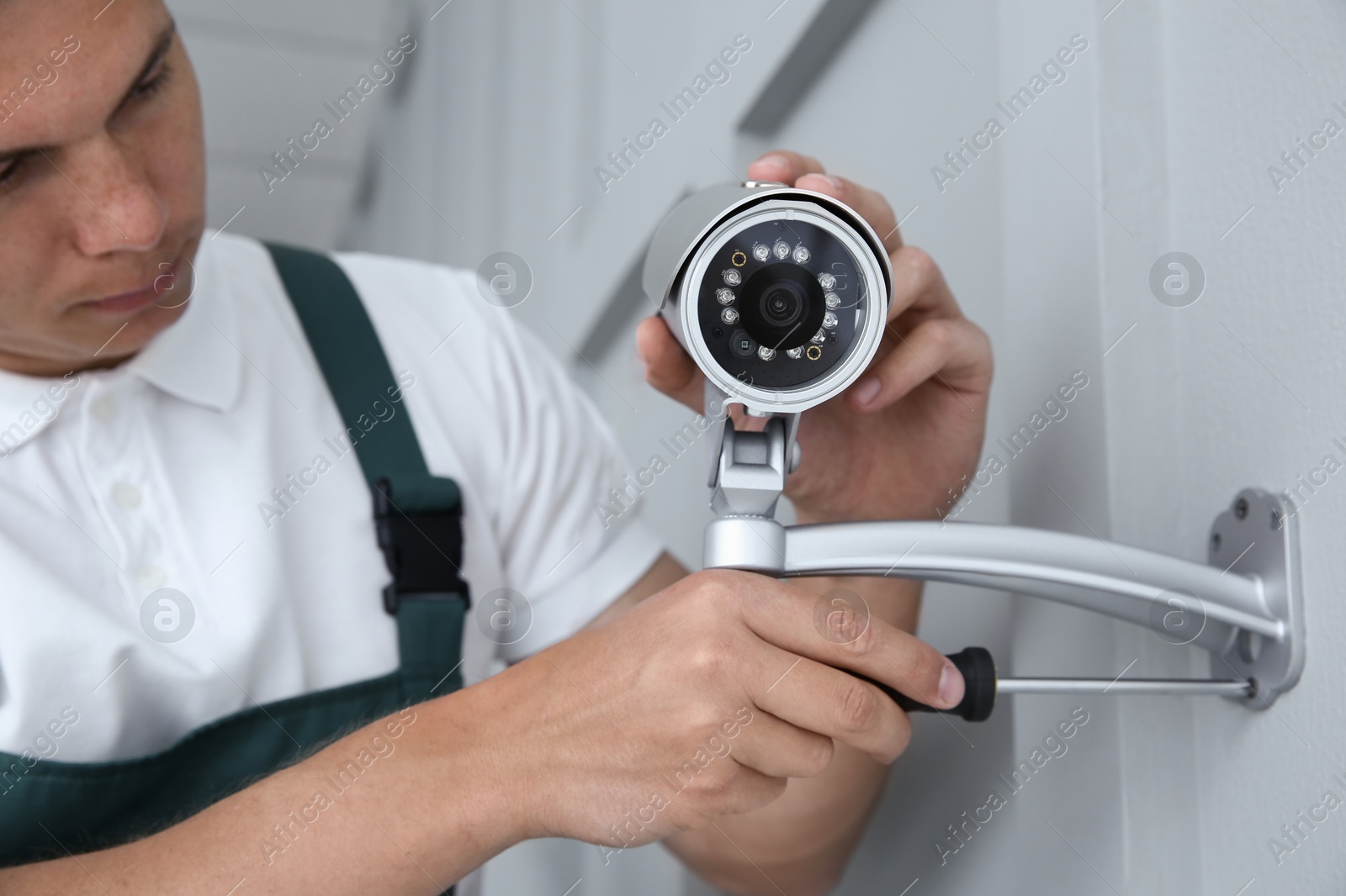 Photo of Technician with screwdriver installing CCTV camera on wall indoors