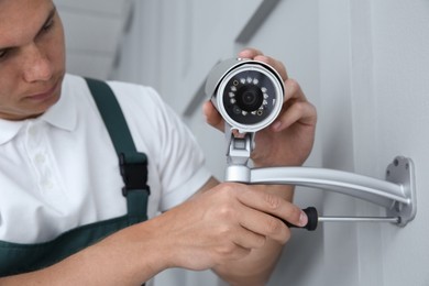 Technician with screwdriver installing CCTV camera on wall indoors