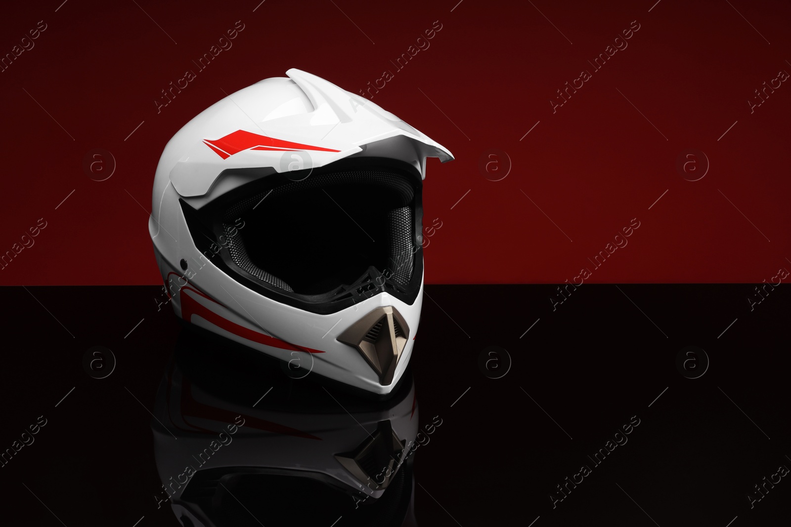 Photo of Modern motorcycle helmet with visor on mirror surface against red background. Space for text