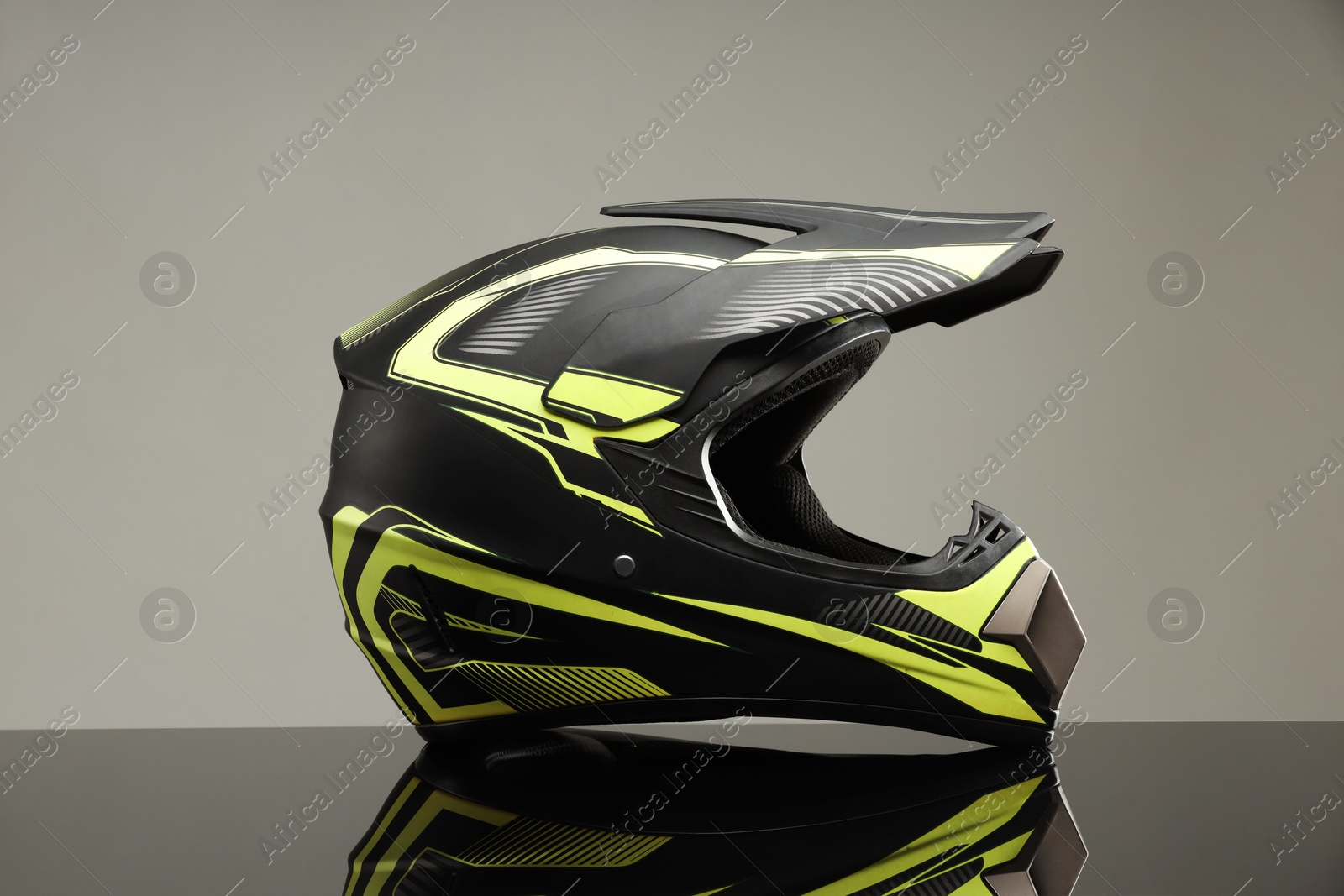 Photo of Modern motorcycle helmet with visor on mirror surface against light grey background