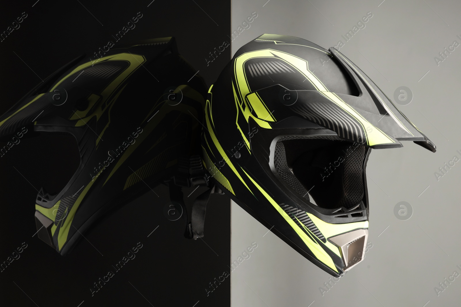 Photo of Modern motorcycle helmet with visor on mirror surface against light grey background