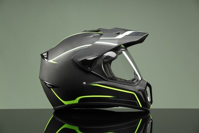 Photo of Modern motorcycle helmet with visor on mirror surface against light grey background