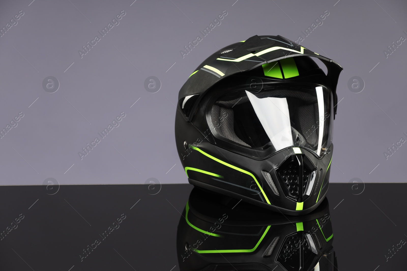 Photo of Modern motorcycle helmet with visor on mirror surface against light grey background. Space for text