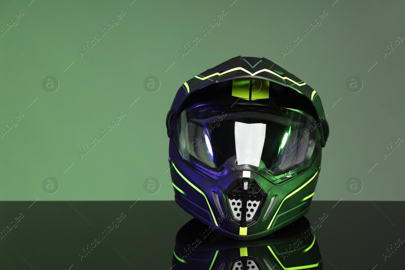 Photo of Modern motorcycle helmet with visor on mirror surface against grey background. Space for text