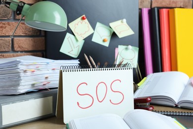 Photo of Notebook with word SOS and stationery on table at workplace