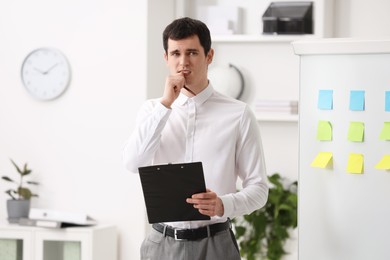 Photo of Embarrassed man with clipboard near white board in office