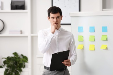 Photo of Embarrassed man with clipboard near white board in office