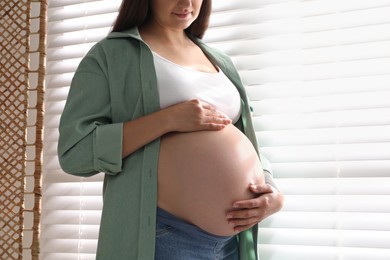 Photo of Pregnant woman near window blinds at home, closeup