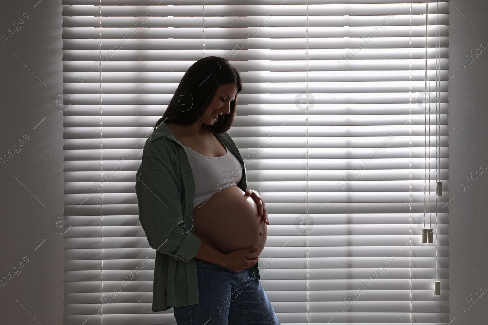 Photo of Beautiful pregnant woman near window blinds at home, closeup. Space for text