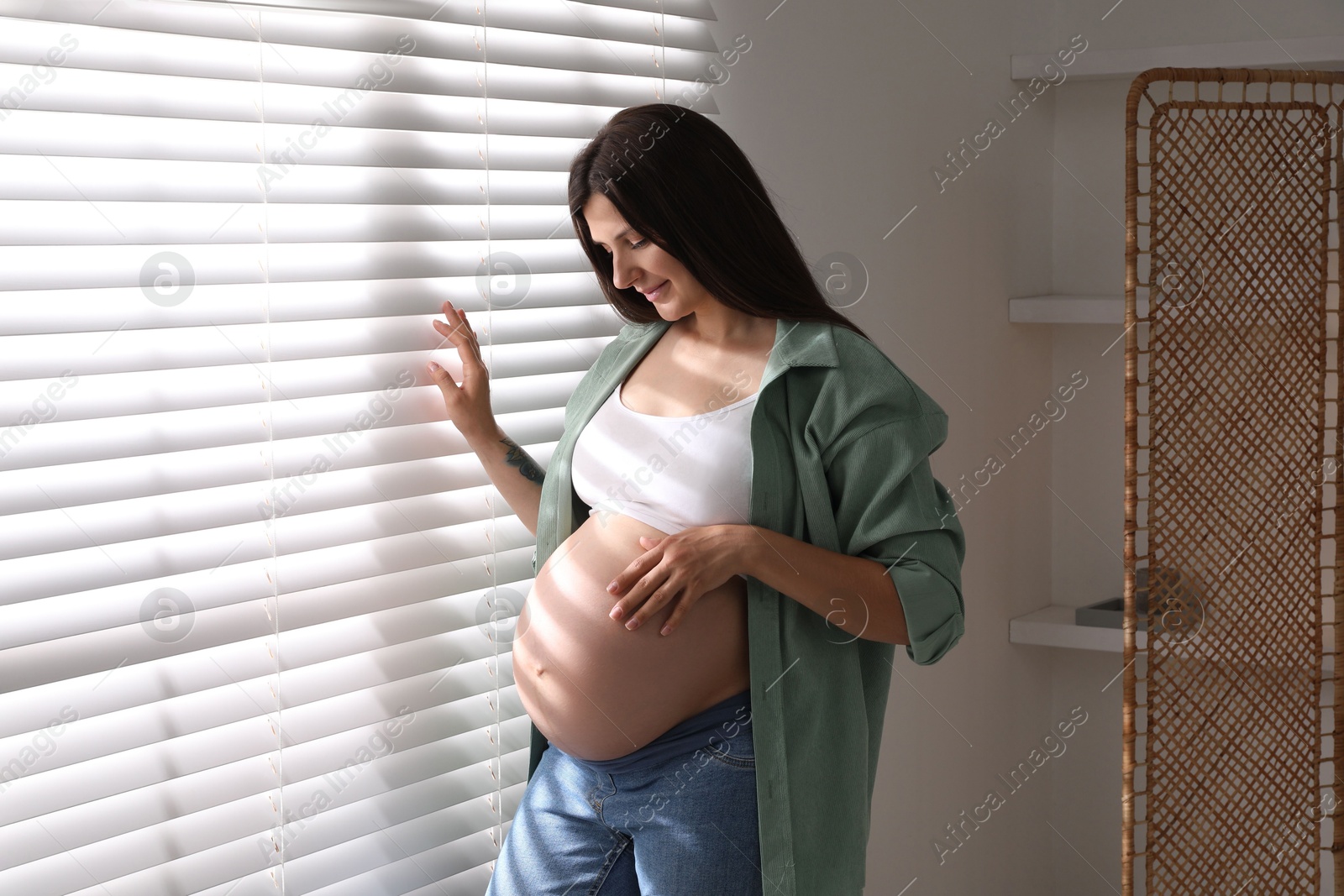 Photo of Beautiful pregnant woman near window blinds at home