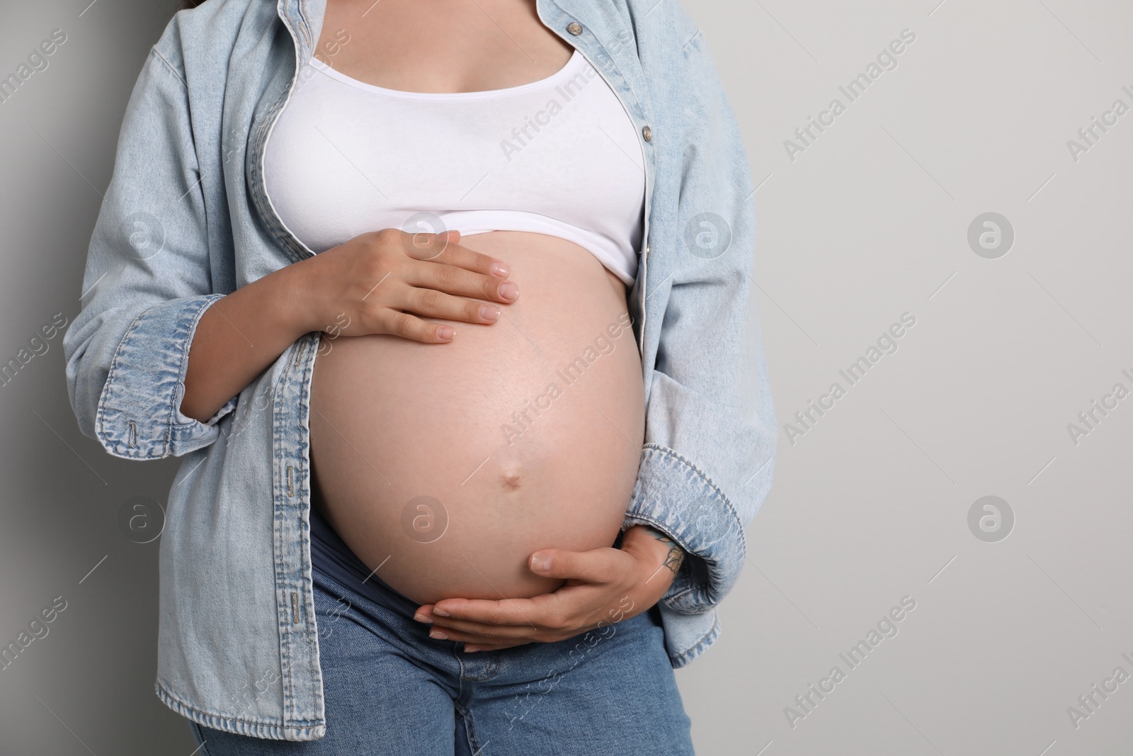 Photo of Pregnant woman on gray background, closeup. Space for text