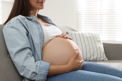 Photo of Pregnant woman sitting on sofa at home, closeup