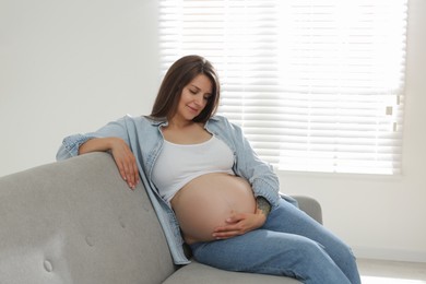 Beautiful pregnant woman sitting on sofa at home