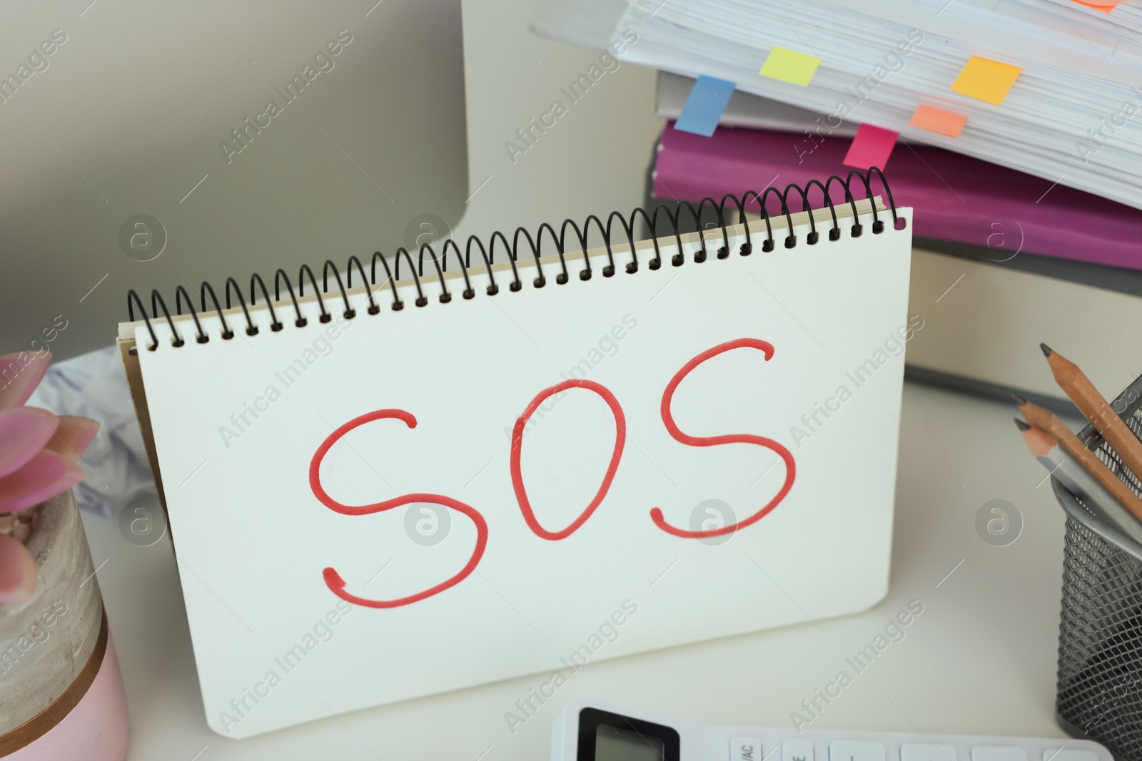 Photo of Notebook with word SOS and stationery on white table at workplace