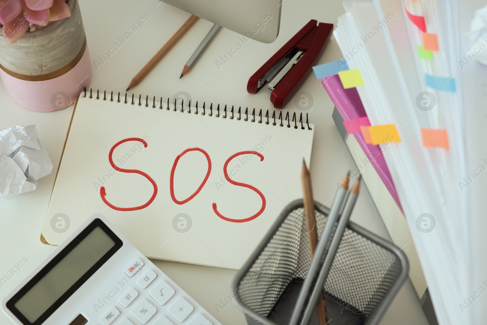 Photo of Notebook with word SOS and stationery on white table at workplace