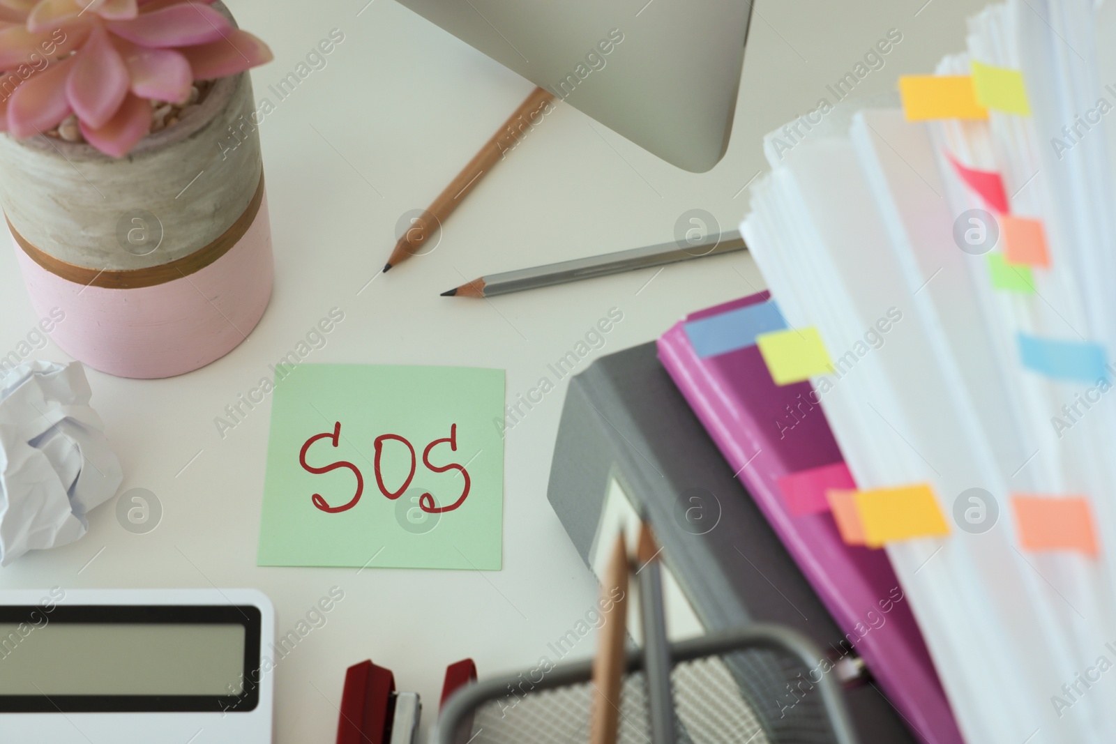 Photo of Note with word SOS and stationery on white table at workplace