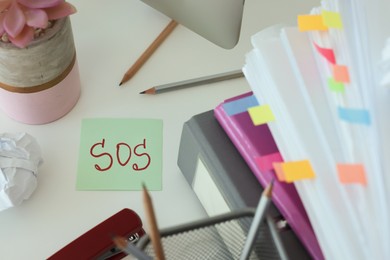 Photo of Note with word SOS and stationery on white table at workplace