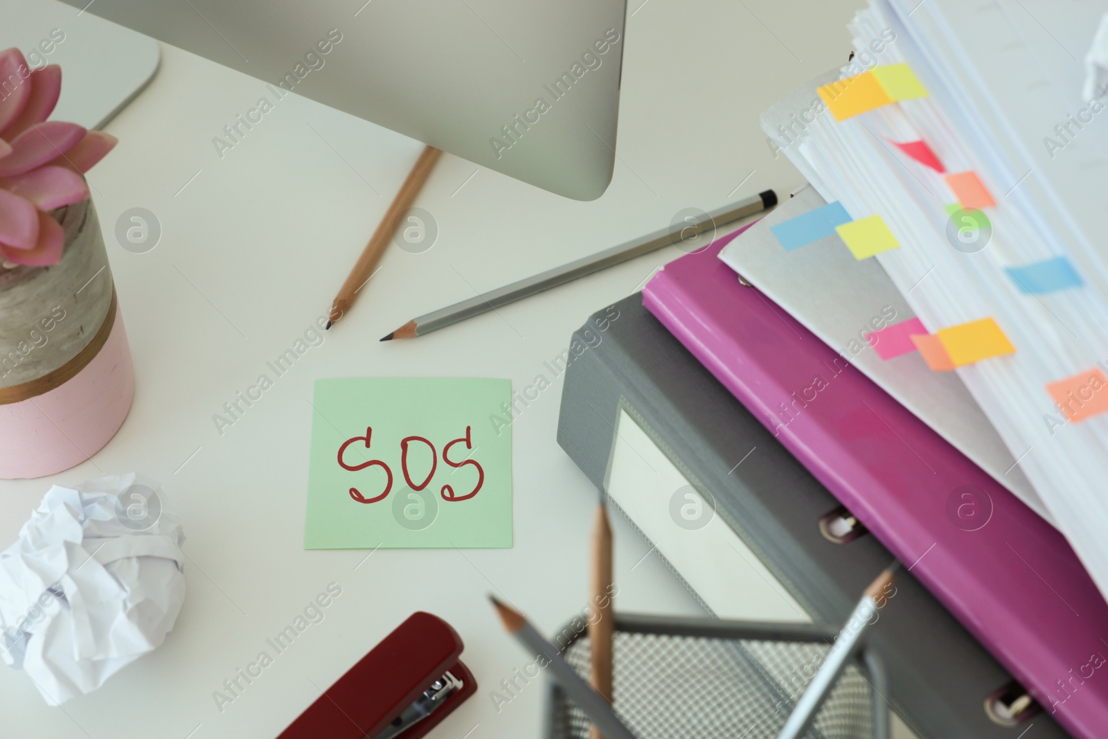 Photo of Note with word SOS and stationery on white table at workplace