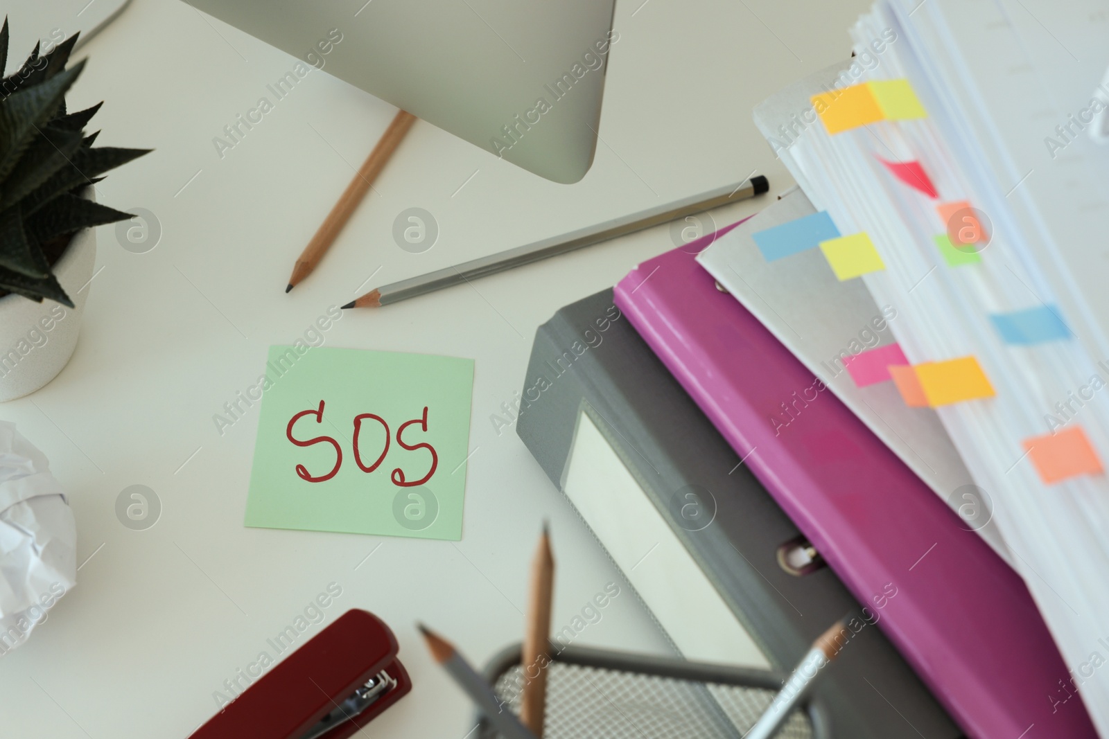 Photo of Note with word SOS and stationery on white table at workplace