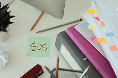 Photo of Note with word SOS and stationery on white table at workplace