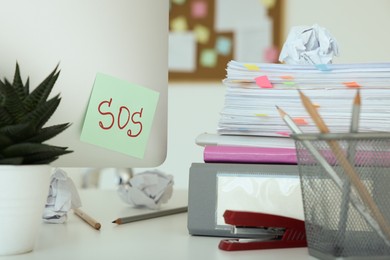 Note with word SOS and stationery on white table at workplace