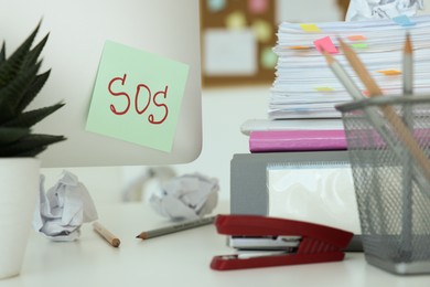 Photo of Note with word SOS and stationery on white table at workplace