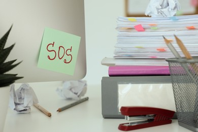 Note with word SOS and stationery on white table at workplace