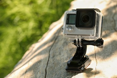 Photo of Modern action camera with mount on wooden surface outdoors, closeup. Space for text