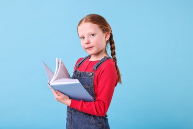 Photo of Cute girl with book on light blue background