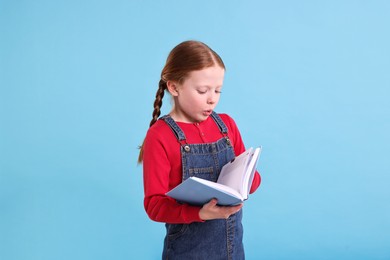 Photo of Cute girl reading book on light blue background