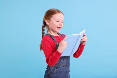 Cute girl reading book on light blue background