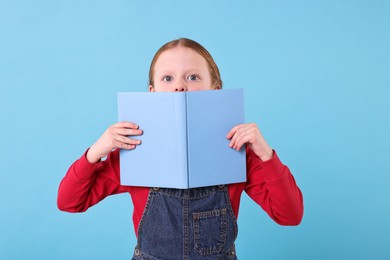 Photo of Cute girl with book on light blue background