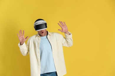 Photo of Surprised man using virtual reality headset on yellow background, space for text