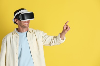 Photo of Smiling man using virtual reality headset on yellow background, space for text