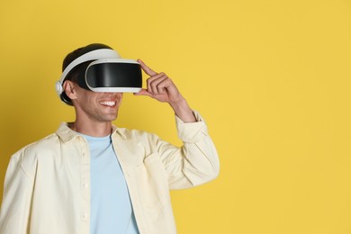 Photo of Smiling man using virtual reality headset on yellow background, space for text