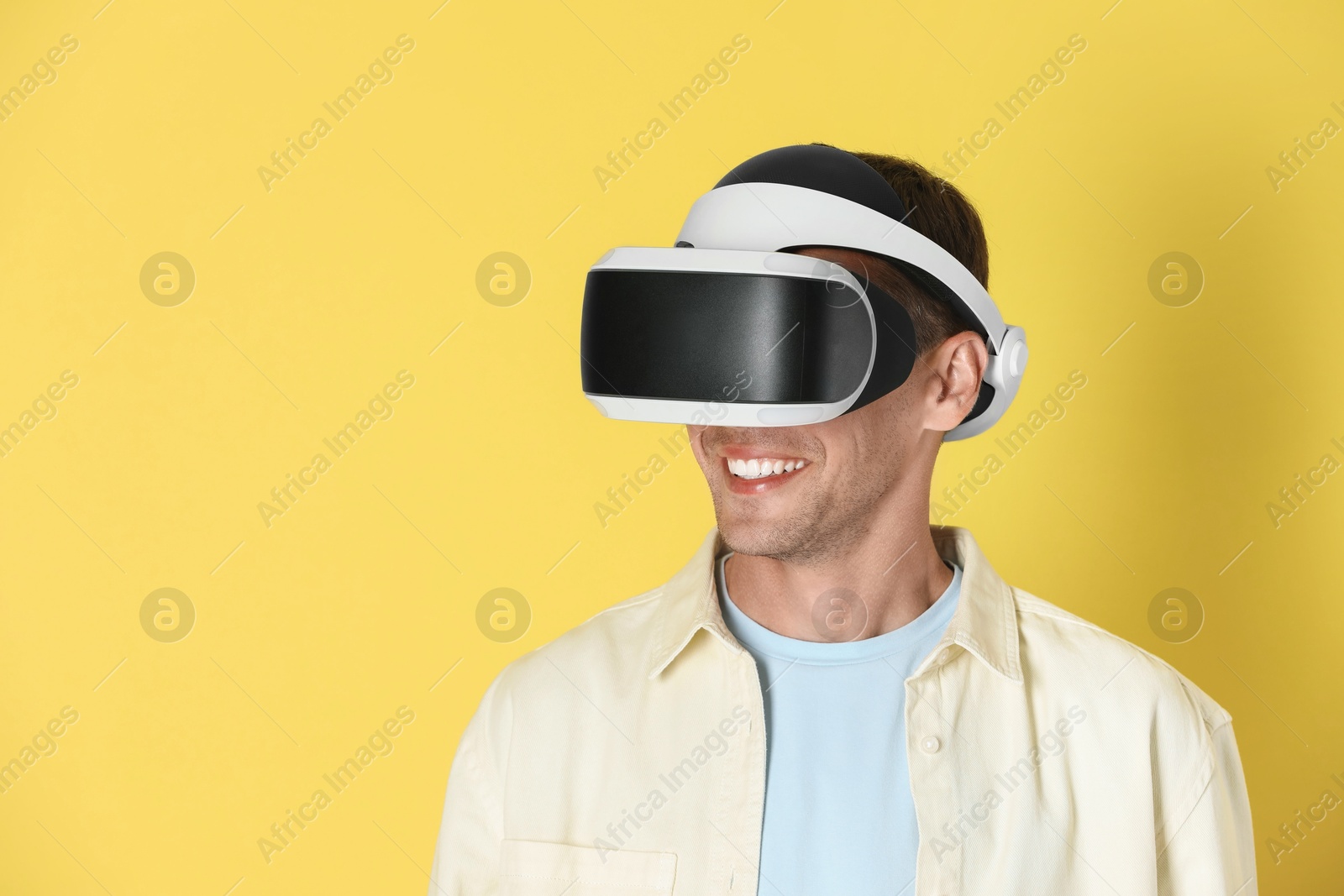 Photo of Smiling man using virtual reality headset on yellow background, space for text