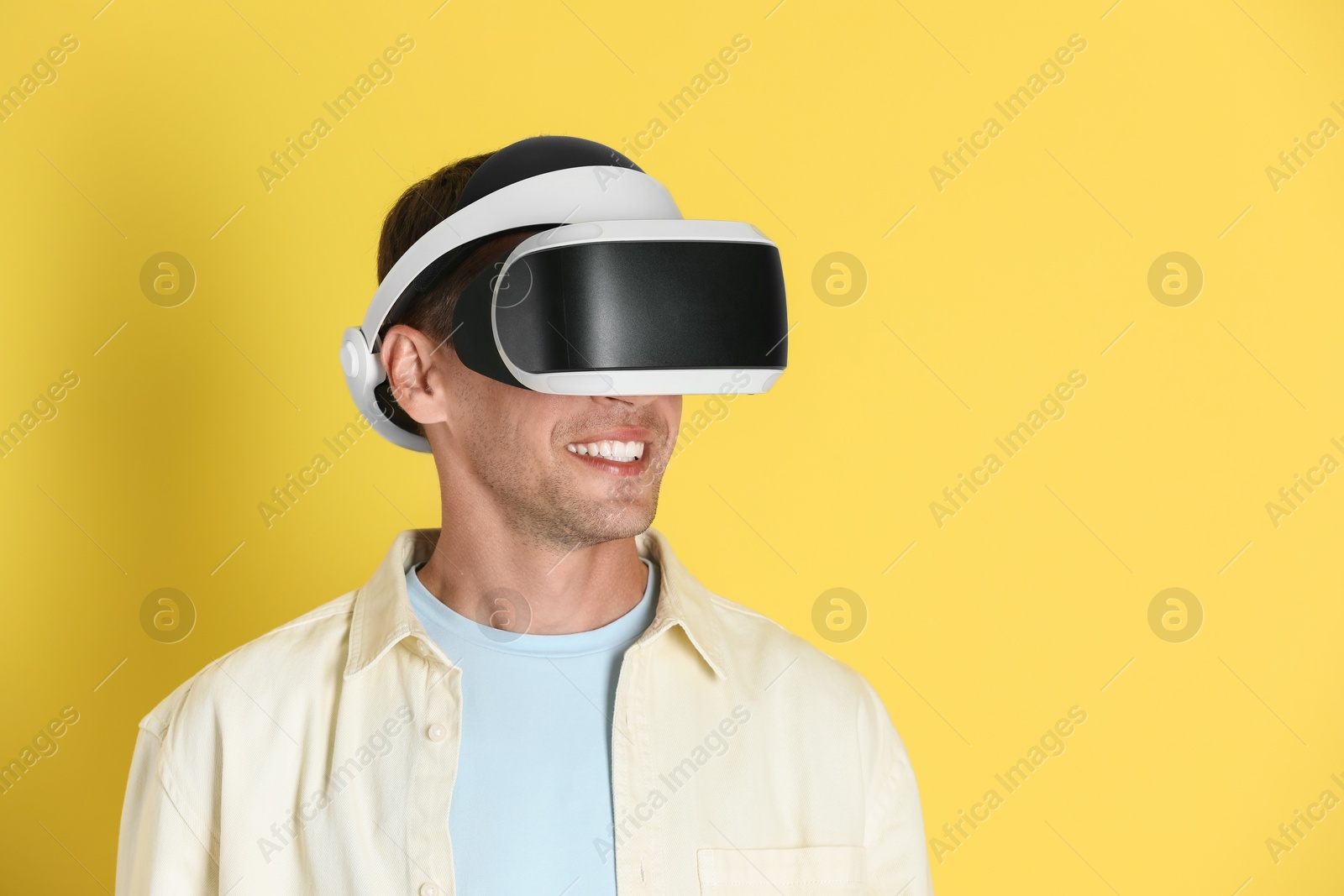 Photo of Smiling man using virtual reality headset on yellow background, space for text