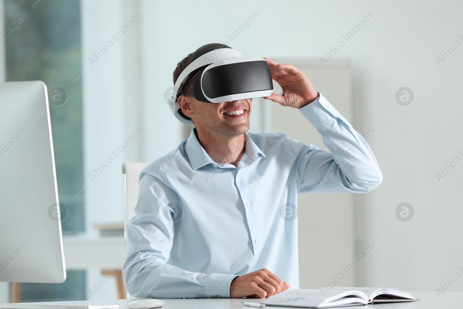 Photo of Smiling man using virtual reality headset in office