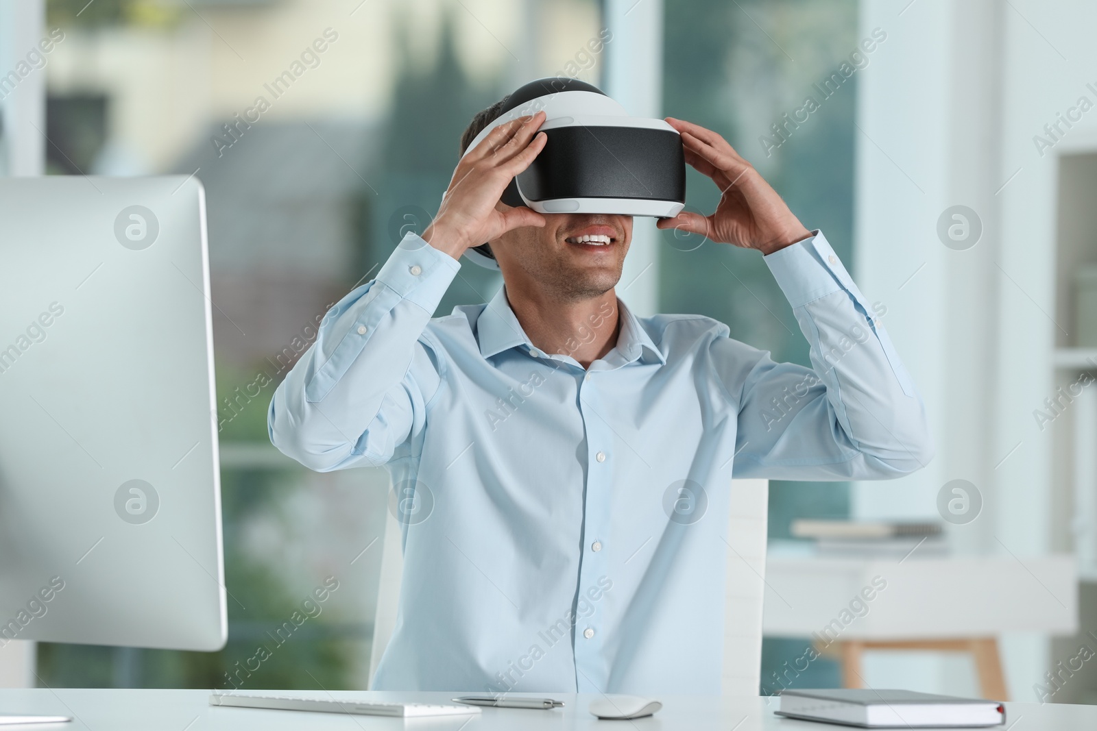 Photo of Smiling man using virtual reality headset in office