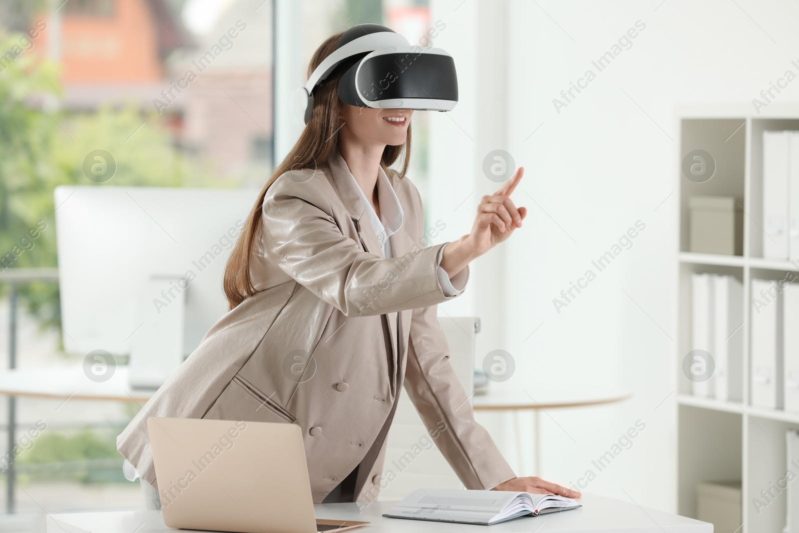 Photo of Smiling woman using virtual reality headset in office