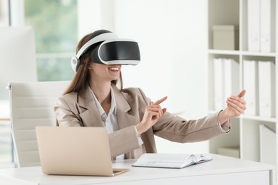 Photo of Smiling woman using virtual reality headset in office