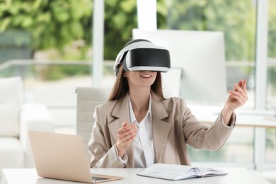 Photo of Smiling woman using virtual reality headset in office
