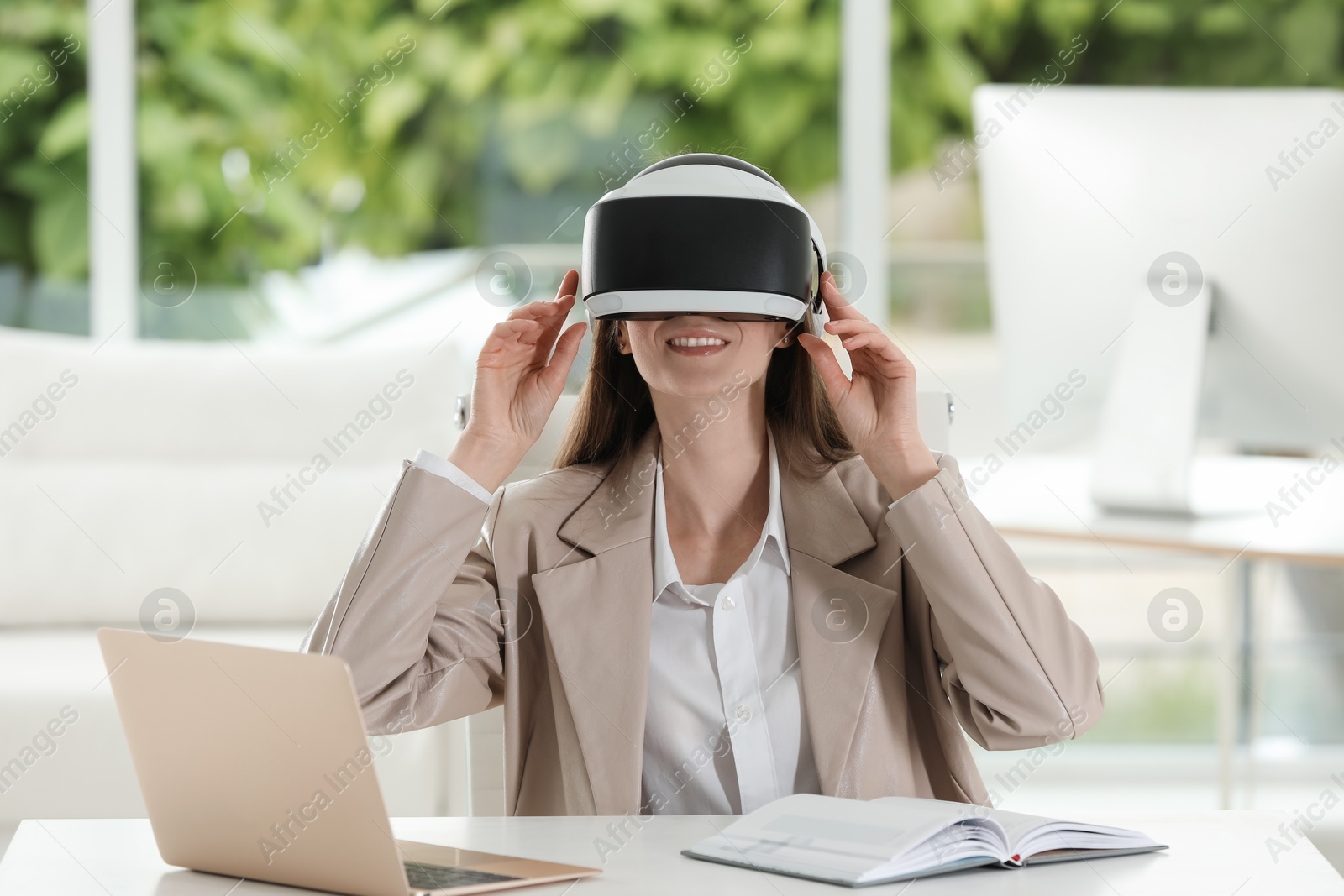 Photo of Smiling woman using virtual reality headset in office