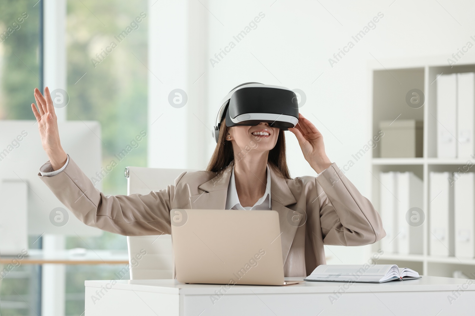 Photo of Smiling woman using virtual reality headset in office