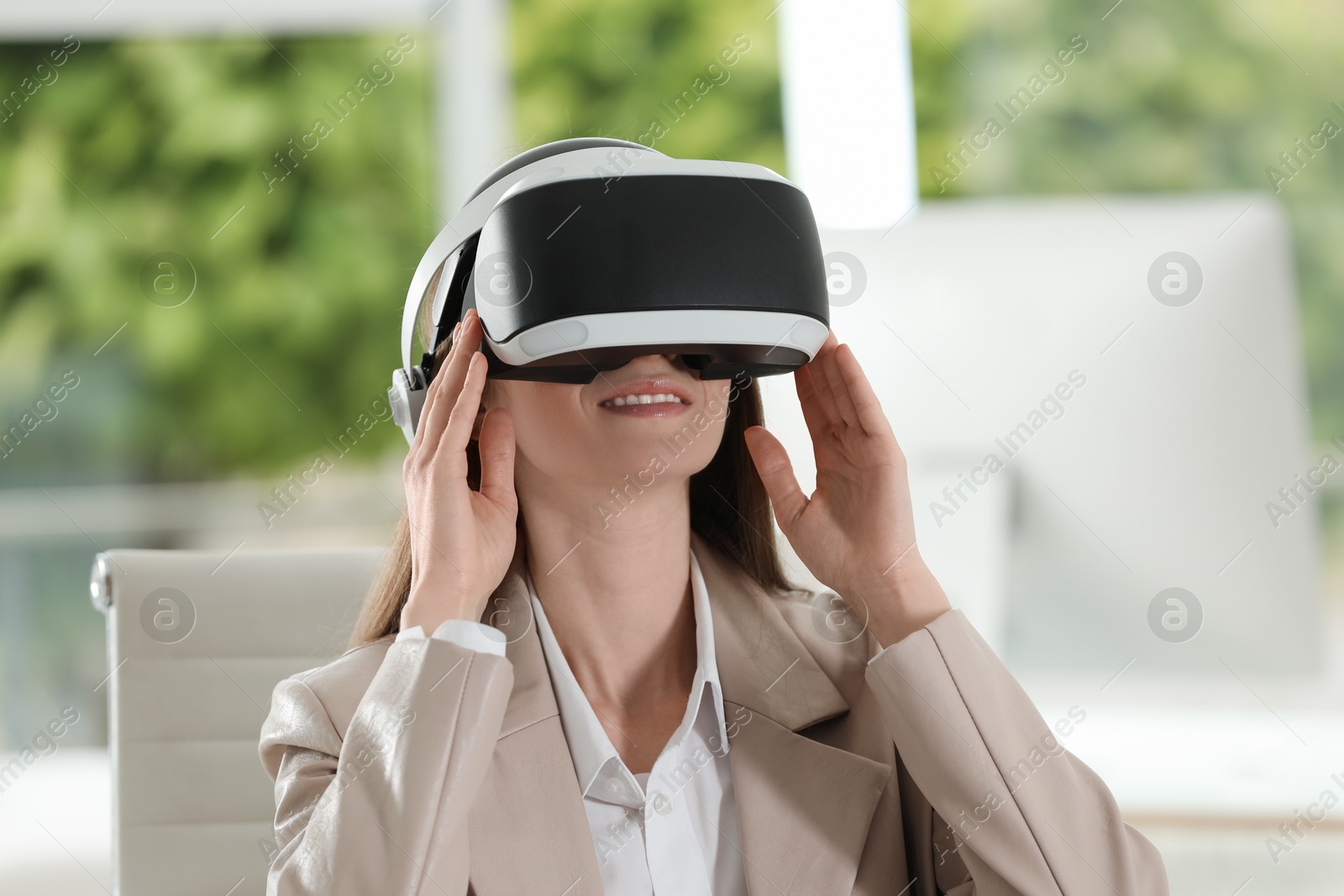 Photo of Smiling woman using virtual reality headset in office